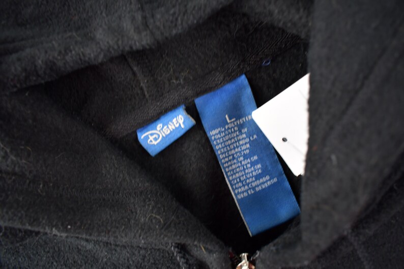 May include: A black hooded sweatshirt with a blue Disney label and a blue care label. The care label lists the fabric as 100% polyester.
