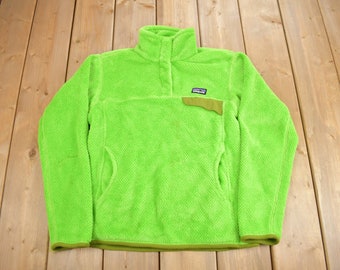 May include: A bright green fleece pullover with a snap button placket and a small logo patch on the left chest. The fleece has a textured, waffle-like pattern.