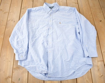 May include: A light blue long-sleeved button-down shirt with a small embroidered logo on the left chest.