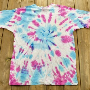 May include: A white t-shirt with a blue and pink tie-dye pattern. The pattern is a swirl design.