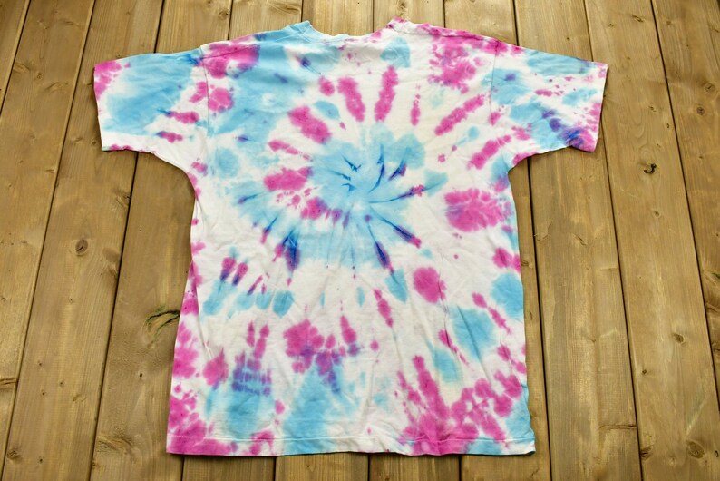 May include: A white t-shirt with a blue and pink tie-dye pattern. The pattern is a swirl design.