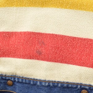 May include: Close-up of a blue denim jacket with a red, white, and yellow striped flannel lining. The jacket has two metal buttons.