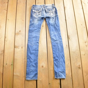 K&ouml;nnte beinhalten: Eine blaue Jeanshose mit silbernen Verzierungen auf den Ges&auml;&szlig;taschen.
