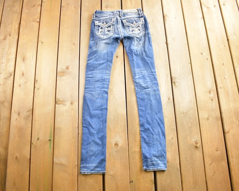 K&ouml;nnte beinhalten: Eine blaue Jeanshose mit silbernen Verzierungen auf den Ges&auml;&szlig;taschen.