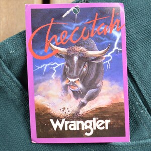 May include: A green pair of Wrangler jeans with a tag that says "Checutah" and features a black bull running through a field with lightning bolts in the background.