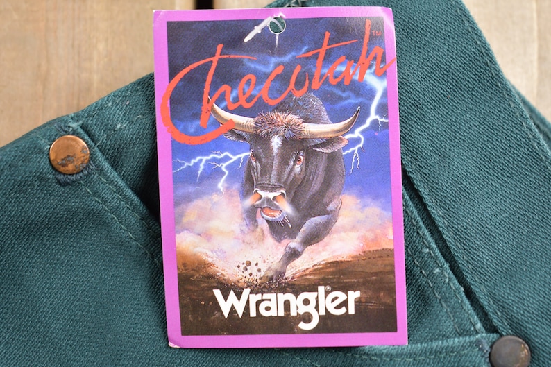 May include: A green pair of Wrangler jeans with a tag that says "Checutah" and features a black bull running through a field with lightning bolts in the background.