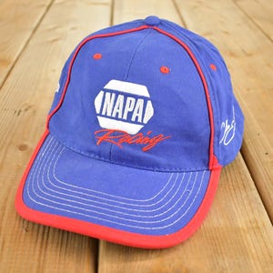 Könnte beinhalten: Blaue Baseballkappe mit rotem Rand und Akzenten. Die Kappe zeigt das NAPA Racing Logo in Weiß und Rot. Der Hut ist aus strapazierfähigem Material gefertigt und hat einen gebogenen Schirm. Ein stilvolles Accessoire für jeden Rennsportfan.