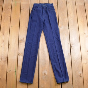 May include: A pair of dark blue denim jeans laid flat on a wooden surface.