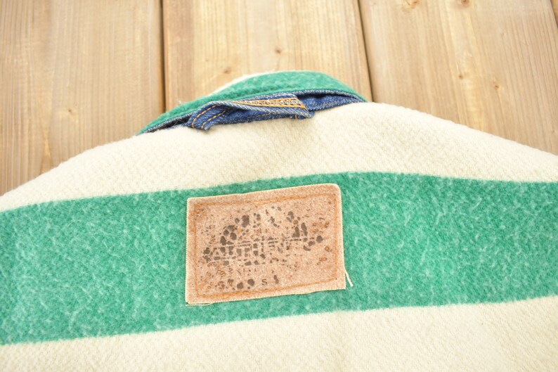 May include: A white and green striped fabric with a brown leather patch. The patch has a logo with the word "ARCTIC" printed on it.