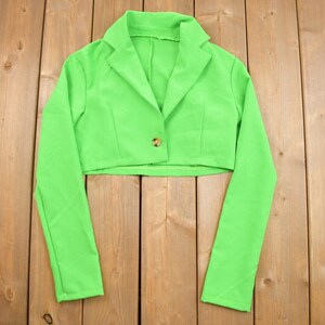 Puede incluir: Una chaqueta corta de color verde brillante con mangas largas y un cierre de botón.