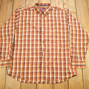 May include: A long-sleeved button-down shirt with a plaid pattern in shades of orange, brown, and white.