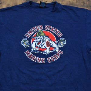 May include: A navy blue t-shirt with a graphic of the United States Marine Corps logo. The logo features a bulldog wearing a military hat and holding a rifle. The words "United States Marine Corps" are written around the logo.