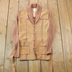 May include: A brown suede and knit jacket with a shawl collar and button closure. The jacket has two pockets and a belt.
