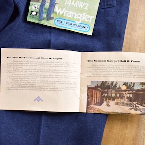 May include: A pamphlet with the text "On The Rodeo Circuit With Wrangler" and "The National Cowgirl Hall Of Fame" on a blue denim background. The pamphlet has a picture of a building with a fountain in front of it.