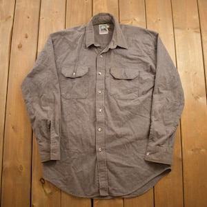 May include: A gray long-sleeved button-down shirt with two chest pockets.