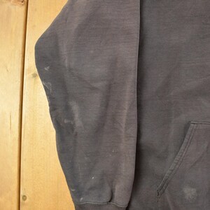 May include: A dark gray hoodie with a front pocket and a drawstring hood. The sleeve is visible, showing some discoloration. The background is a light brown wooden surface.