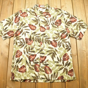 May include: A white short-sleeved shirt with a brown and green floral pattern. The shirt has a button-up front and a collar.