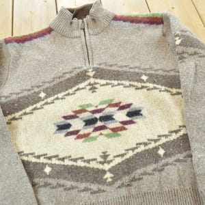 Peut inclure: Un pull gris zipp&eacute; avec un motif g&eacute;om&eacute;trique au centre. Le motif comprend des losanges cr&egrave;me, marron, noirs, rouges et verts. Le pull a un ourlet et des poignets c&ocirc;tel&eacute;s.