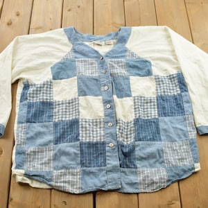 May include: A white long-sleeved button-up shirt with a patchwork design. The patchwork is made of blue and white checkered fabric.