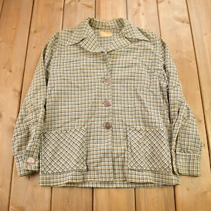 May include: A plaid button-up shirt with two pockets and a collar. The shirt is a light brown and black color.