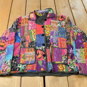 May include: A long-sleeve jacket featuring a vibrant patchwork design with various colourful patterns including floral, geometric, and abstract prints. The jacket has a collared neckline, a front button closure with five black buttons, and two front pockets.