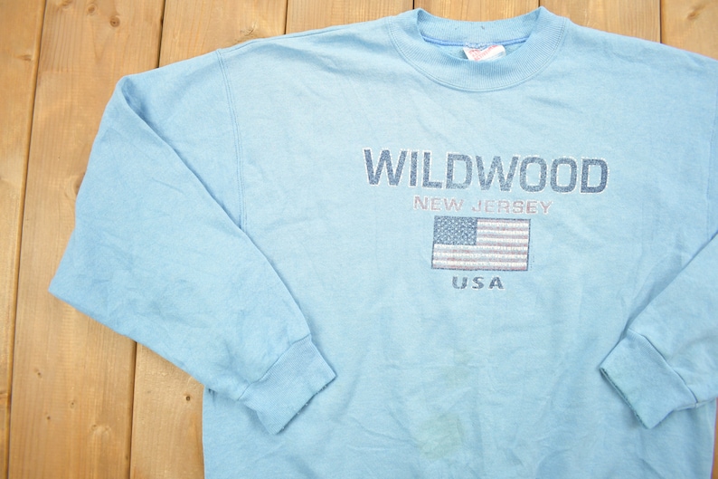 May include: Light blue long-sleeved sweatshirt with the text "WILDWOOD NEW JERSEY USA" and a small American flag graphic.
