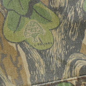 May include: Close-up of a camouflage fabric with a pattern of green, brown, and gray shapes. The word "POLAR" is visible within the design. The fabric appears to be denim or a similar sturdy material.