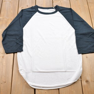 Op de afbeelding: Een wit en donkerblauw baseball T-shirt met een gebogen zoom. Het shirt heeft driekwart mouwen.