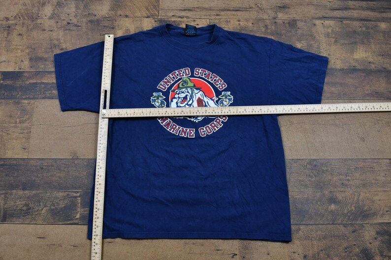 May include: A navy blue t-shirt with a graphic of a cartoon bulldog wearing a military hat. The graphic is surrounded by the text "United States Marine Corps".