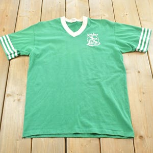May include: Green v-neck t-shirt with white stripes on the sleeves and collar. The shirt features a white graphic on the chest that reads "Rockford Bike Club". The t-shirt is made of a soft material.