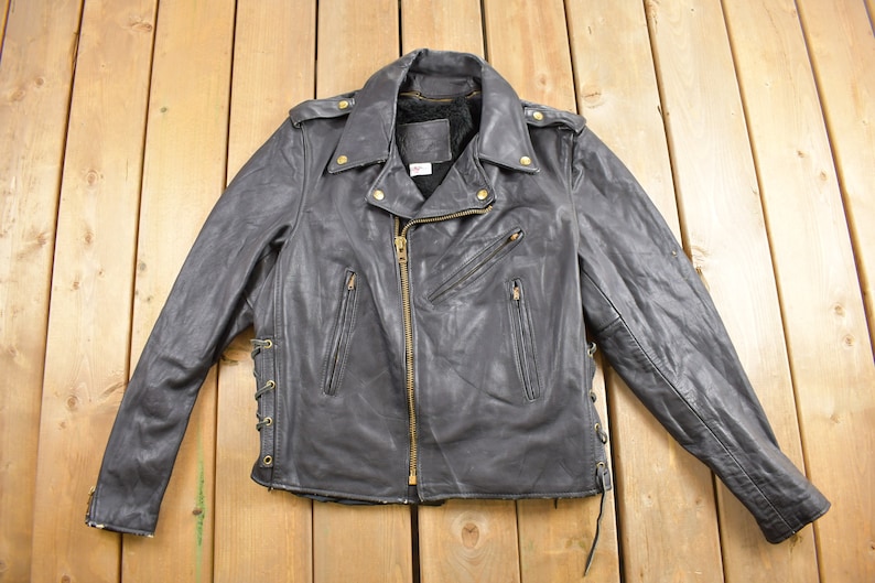 May include: Black leather motorcycle jacket with a zipper closure, side pockets, and a lace-up detail on the sides.
