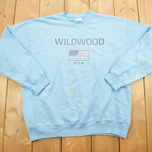 May include: A light blue sweatshirt with the text "WILDWOOD NEW JERSEY USA" and an embroidered American flag.