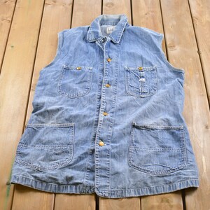 Può includere: Un giubbotto di jeans blu chiaro con chiusura a bottoni, quattro tasche e un aspetto sbiadito.