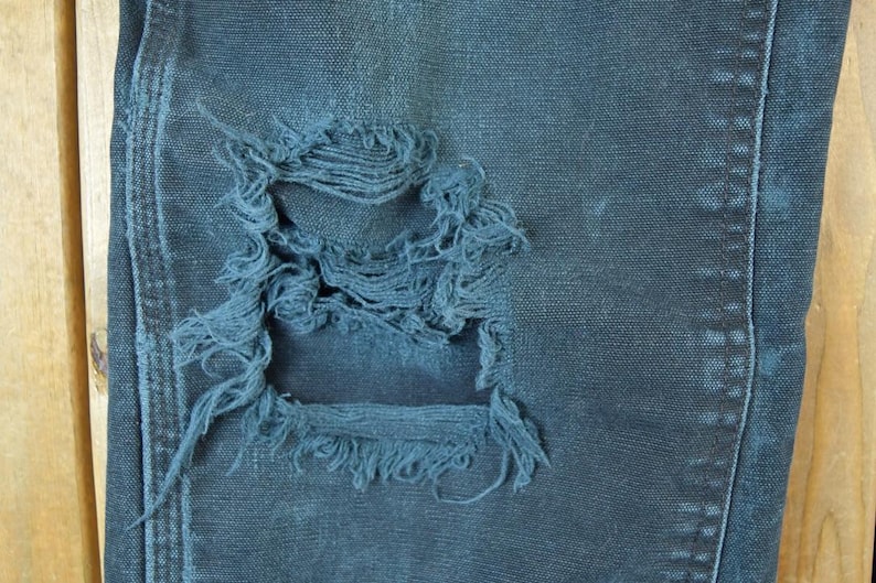 May include: Close-up of distressed denim jeans in a dark blue wash. The jeans feature a large, frayed hole, showcasing the fabric's texture and wear. The image highlights the details of the ripped design.