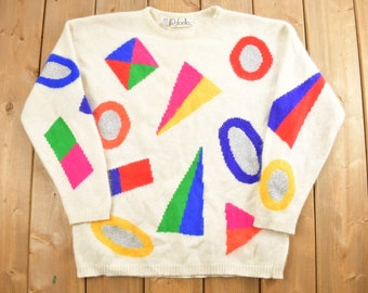 May include: A white knitted sweater with a geometric pattern in bright colors, including red, blue, green, yellow, and pink. The sweater has a crew neck and long sleeves.