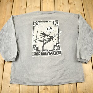 Puede incluir: Sudadera gris de manga larga con un gr&aacute;fico de Jack Skellington de The Nightmare Before Christmas, con el texto "BONE DADDY" debajo. Las mangas tienen un dise&ntilde;o texturizado y acanalado.