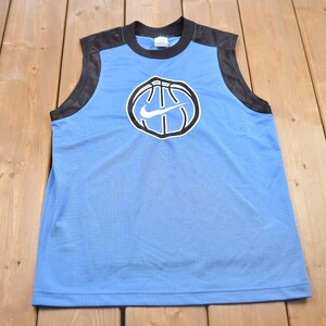 May include: A light blue sleeveless basketball jersey with black mesh side panels. The front of the jersey features a black and white basketball with a white Nike swoosh logo.