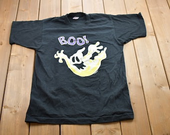 Peut inclure: T-shirt noir avec un motif de fantôme jaune et violet et le mot "BOO!" imprimé dessus.