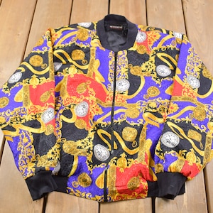 May include: A vintage bomber jacket with a vibrant pattern. The jacket features a black base with a repeating design of gold, red, and purple baroque-style elements. It has a black collar, cuffs, and hem, and a full-length zipper.