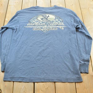 May include: A light blue long-sleeve shirt with a graphic on the back. The graphic features a surfer and the words "Hawaiian Legends Classic Longboards". The shirt is made of a soft material.
