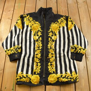 May include: A black and white striped jacket with gold floral embroidery. The jacket has a zip fastening and long sleeves.
