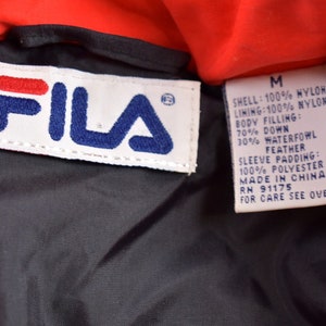 May include: A red Fila jacket with a black lining. The label says "SHELL: 100% NYLON LINING: 100% NYLON BODY FILLING: 70% DOWN 30% WATERFOWL FEATHER SLEEVE PADDING: 100% POLYESTER MADE IN CHINA RN 91175 FOR CARE SEE OVER"