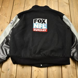 Könnte beinhalten: Schwarze Collegejacke mit Lederärmeln. Auf der Rückseite der Jacke befindet sich ein Aufnäher mit der Aufschrift "FOX NFL SUNDAY".