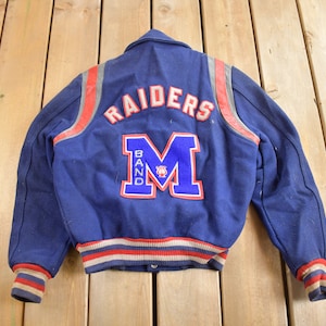 May include: A blue varsity jacket with red and white stripes on the sleeves and bottom. The back of the jacket has the word "RAIDERS" in white letters and a blue "M" with the word "BAND" in red letters.