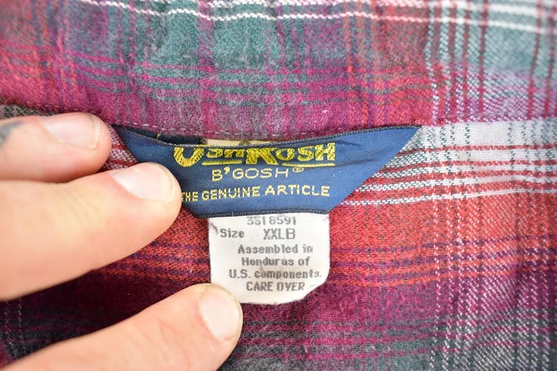 Puede incluir: Primer plano de una etiqueta de camisa a cuadros. La etiqueta dice "Van Kosk B'Gosh The Genuine Article" con la talla XXLB. La camisa es una mezcla de cuadros rojos, verdes y blancos.