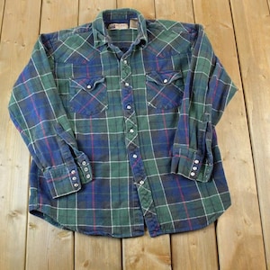 May include: A long-sleeved plaid shirt with a green, blue and red plaid pattern. The shirt has a button-down collar, a button-up front and two chest pockets.