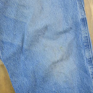 May include: Close-up of a light blue denim fabric with a subtle texture. The fabric has a slightly faded appearance, indicating it is well-worn.