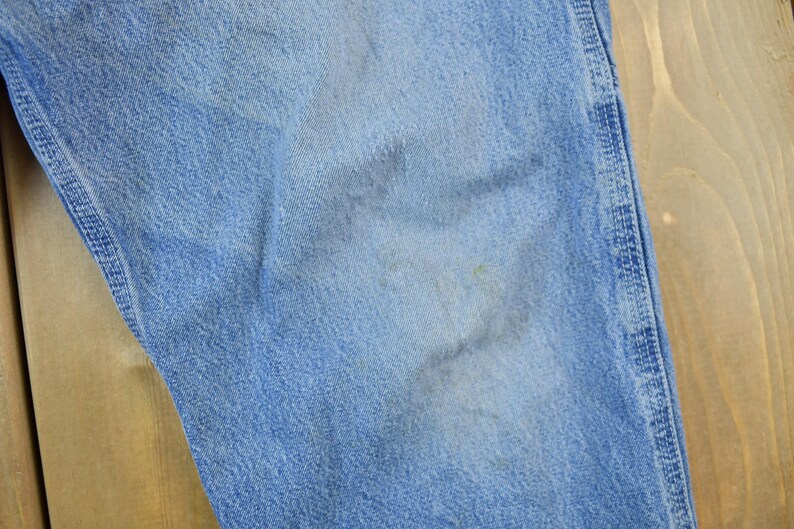 May include: Close-up of a light blue denim fabric with a subtle texture. The fabric has a slightly faded appearance, indicating it is well-worn.