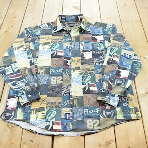 Puede incluir: Una camisa de manga larga con botones y un diseño de patchwork multicolor con varios estampados gráficos, incluyendo el texto Phat, Phat Farm y el número 92. La camisa tiene un cuello estándar, puños abotonados y un cierre frontal de botones.