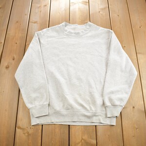 May include: A plain, light grey sweatshirt with long sleeves and a crew neck.